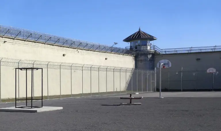 Secure prison yard with high fencing, surveillance tower, and recreational equipment.